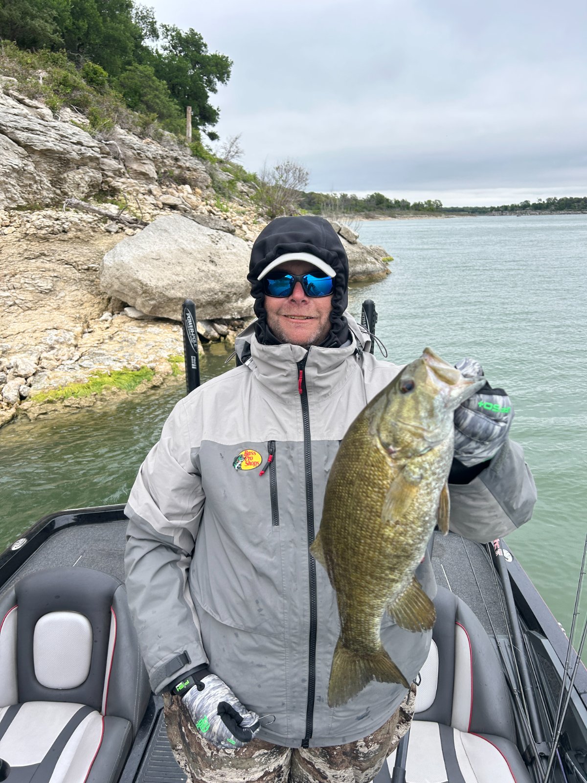 An angler in cold-weather gear with a smallmouth bass against the rock bluffs of Lake Belton