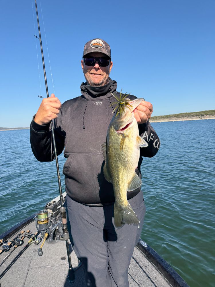 An angler on the bow of the boat holding up a largemouth bass on Canyon Lake
