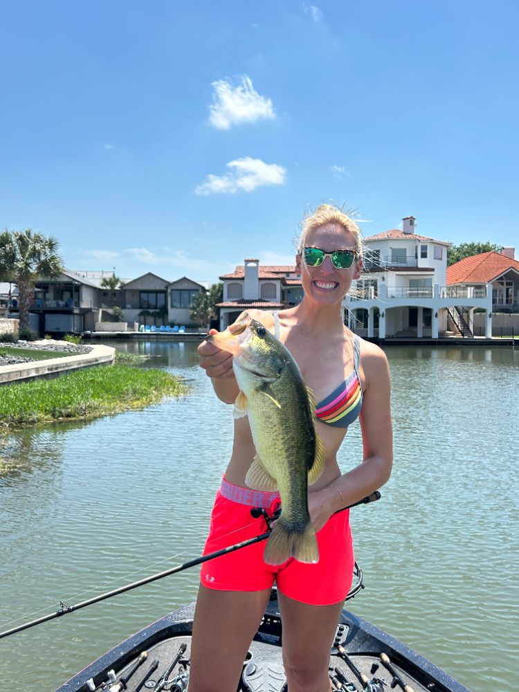 An angler holding a largemouth bass in front of the waterfront homes on Lake LBJ